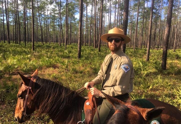 Jesse, on a horse in a clearing, smiling at the camera.